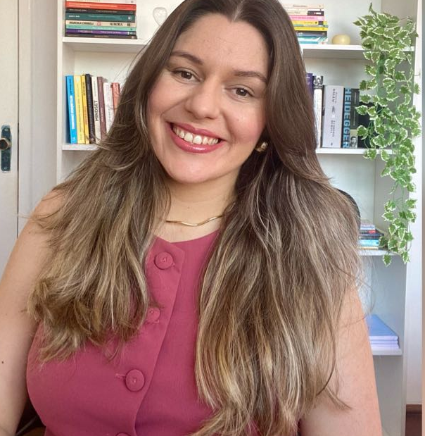 Vivane Menezes, psicóloga, sorrindo com estante de livros ao fundo
